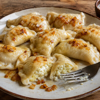 Traditional Polish pierogi filled with potato and twaróg, served with golden onions and sour cream